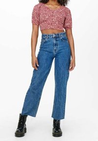 Rotes, floral gemustertes Cropped-Top mit kurzen Ärmeln, kombiniert mit hohen, weiten blauen Jeans und schwarzen Schnürstiefeln.
