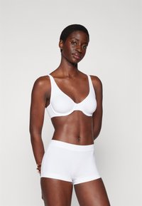 White seamless bra with adjustable straps paired with matching shorts. Smooth fabric and minimalist design with no visible hardware or patterns.