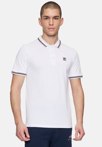 Vit polo t-shirt med korta ärmar, kontrasterande marinblå och röda randiga krage och ärmslut, samt en liten broderad logotyp på bröstet.