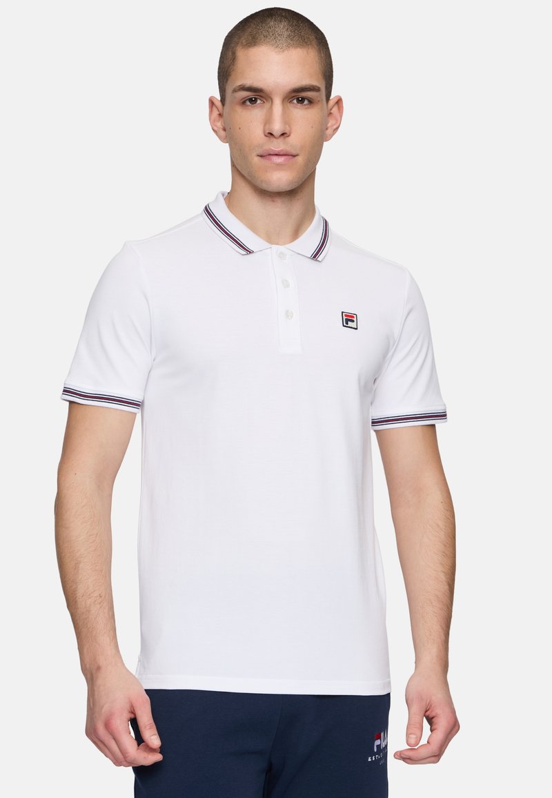 Vit polo t-shirt med korta ärmar, kontrasterande marinblå och röda randiga krage och ärmslut, samt en liten broderad logotyp på bröstet.