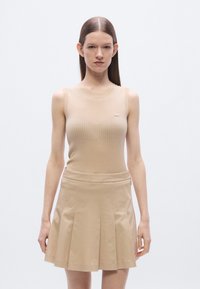 Top sin mangas beige acanalado combinado con una falda plisada a juego, con un detalle sutil de logo en el top. Textura suave, diseño ajustado.