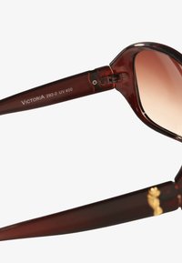 Okulary przeciwsłoneczne z ciemnobrązowymi, błyszczącymi plastikowymi oprawkami oraz gradientowymi soczewkami; mają metalowe zawiasy i mały złoty akcent na zausznicy.