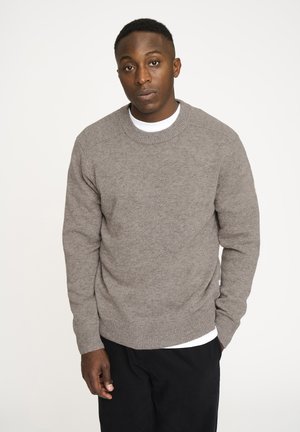 Grå striktrøje med rund hals, ribbede manchetter og kant. Båret over en hvid T-shirt ser stoffet blødt og tekstureret ud.