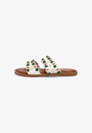 Sandalia blanca de cuero tipo slide con dos tiras con bordes ondulados decoradas con tachuelas redondas verdes y doradas y una suela plana marrón.