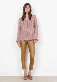 Punane ja valge muster piknikäisel blousee, millel on nupploot, koos sobivate beežide kunstnahast pükste ja pruunide sussidega.