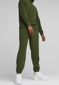 Olivgrüner Fleece-Trainingsanzug mit hohem Kragen, gerippten Bündchen und schmal zulaufenden Hosen, kombiniert mit weißen Plateausneakern.