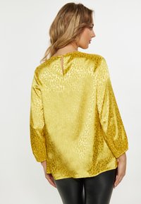 Yellow satin blouse with a leopard print pattern, 3/4 sleeves, a keyhole back detail, and a relaxed fit, paired with black leggings.