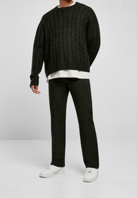 Suéter de punto grueso en verde oscuro, superpuesto a una camisa blanca, combinado con jeans negros y zapatillas blancas. Diseño sencillo, tejido texturizado.