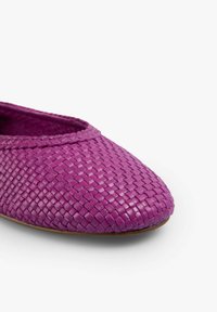 Zapato plano tejido en color púrpura, con punta redondeada, superficie texturizada y forro suave, diseñado para ofrecer comodidad y facilidad de uso.