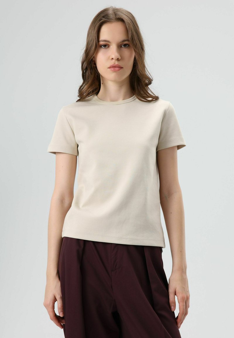 Beige short-sleeve t-shirt with a round neckline, made from smooth fabric, paired with loose dark burgundy pants.