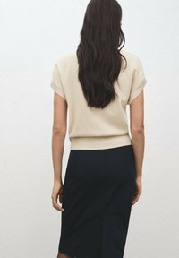 Beige stickad topp med kort ärm kombinerad med en figursydd svart kjol. Slät yta, enkel design, med en lätt ribbad fåll och rena linjer.