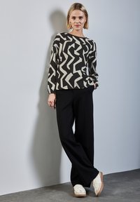 Haut à manches longues noir et blanc à motif zigzag, associé à un pantalon large noir et des baskets blanches avec des accents marron.