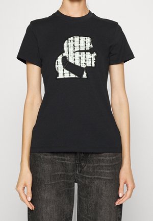 Schwarzes kurzärmeliges Hemd mit einem weißen, strukturierten Grafikbild eines seitlichen Profils einer Person mit Sonnenbrille und hohem Kragen, getragen zu dunklen Jeans.