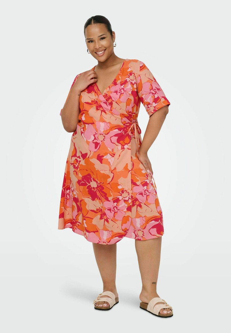 Floral wrap dress in orange and pink tones. Short sleeves, knee-length, with a tie at the side. Smooth fabric with a vibrant flower pattern.