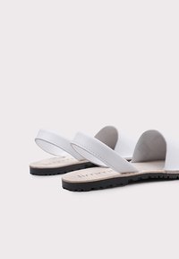 Sandalias de cuero blanco con correas dobles y suela de goma negra. La plantilla es beige con un acabado texturizado y el logotipo de la marca.