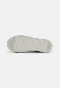 Bijela potplat tenisica s teksturiranim gumenim materijalom. Sadrži izbočine za bolje prianjanje i utisnuti logo "Calvin Klein". Dizajn s zaobljenim petom.