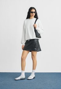 Γυναίκα που φοράει μαύρα γυαλιά ηλίου, υπερμεγέθη ανοιχτογκρι φούτερ, μαύρη δερμάτινη μίνι φούστα, λευκές κάλτσες, ασημένια παπούτσια και κρατάει μαύρη τσάντα ώμου.