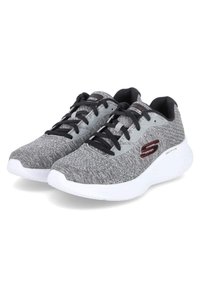 Zapatos deportivos texturizados en gris con acentos negros, que cuentan con una suela blanca acolchada y cordones negros. Logotipo visible en el costado.