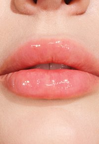 Labbra lucide e piene in una tonalità di rosa morbido con una lucentezza naturale, che mette in risalto la texture liscia e i contorni sottili. Il tono della pelle è uniforme e chiaro.
