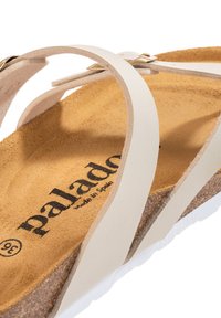Beige sandaler med korksåler har hvide læderstropper og en struktureret brun indersål, mærket med "palado, lavet i Spanien."