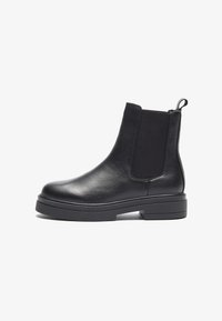Botas de cuero negras hasta el tobillo con paneles elásticos laterales, punta redondeada y suela gruesa negra. Incluyen un tirador en la parte posterior para facilitar su uso.