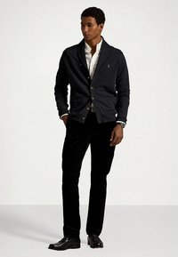 Ναυτικό ζακέτα με ανοιχτόχρωμα κουμπιά, λευκό πουκάμισο με γιακά, μαύρο βελούδινο παντελόνι και μαύρα παπούτσια. Κομψή εφαρμογή με υφασμάτινη υφή.