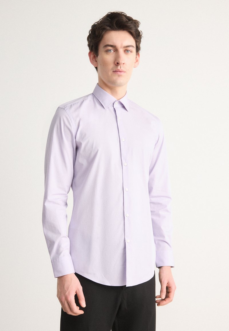 Cămașă lavandă cu nasturi, cu guler ascuțit, mâneci lungi și o textură netedă, băgată în pantaloni negri. Design minimalist.