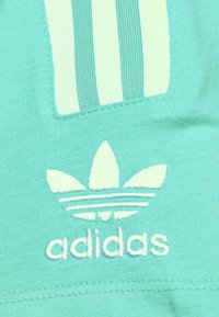 Tela de color verde azulado claro con el logo blanco de trébol de Adidas y tres rayas verticales cosidas encima.