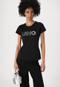 Black t-shirt made of cotton, featuring a round neckline, short sleeves, and silver sequin logo "LIU•JO" on the front.