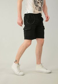 Pantaloni cargo neri con tasche laterali e cintura regolabile con cordino, indossati con sneakers bianche alte, che mostrano un design casual.