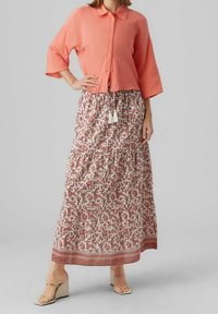 Camisa de botones en color coral con una tela texturizada, combinada con una falda maxi de estampado floral que presenta detalles de volantes y un dobladillo decorativo.