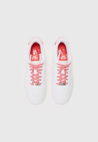 Par vit Nike Air Force 1-sneakers med röda och vita snören och röda innersula, sedd ovanifrån på en vit bakgrund.