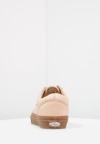 Baskets Vans beiges vues de dos avec semelle en caoutchouc marron et logo "Vans Off The Wall" sur la languette du talon sur fond blanc.