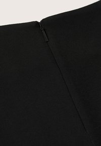 Gros plan sur une fermeture éclair noire fermée sur un tissu noir texturé, montrant le tirette de la fermeture éclair et le détail des coutures.