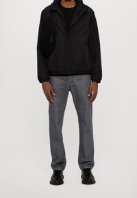 Černá bunda na zip s kapucí, nošená přes černé tričko; světle šedé džínové kalhoty; černé tenisky; malá černá kabelka přes rameno.