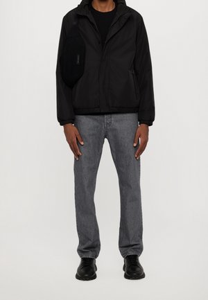 Sort lynlåstrøje med hætte, båret over en sort skjorte; lysegrå denimjeans; sorte sneakers; lille sort crossbody-taske.