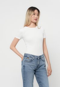 Λευκή εφαρμοστή μπλούζα με κοντά μανίκια, ριμπ υφή, στρογγυλή λαιμόκοψη, συνδυασμένη με ανοιχτό μπλε τζιν παντελόνι ψηλής μέσης με ετικέτα επωνυμίας.