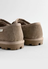 Bottes en suède beige à enfiler, avec une doublure douce, une semelle en caoutchouc épaisse avec des rainures et des accents cousus autour du col.
