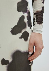 Langärmeliges Kleid aus leichtem Stoff mit beige Grundfarbe und großen dunkelbraunen und lila abstrakten Flecken. Nahtdetails sind in der Nähe des Handgelenks sichtbar.