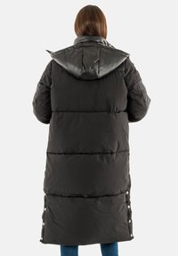 Lange zwarte pufferjas met een gequiltde textuur, afneembare glanzende zwarte capuchon, drukknoopsluiting aan de onderkant en zijzakken.
