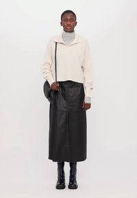 Krämmössa i stickad, grå turtleneck under, kombinerad med en lång svart läderskjol. Svarta ankelboots. Minimalistisk design.