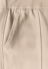 Tessuto beige con un motivo testurizzato, caratterizzato da delicate pieghe e una tasca laterale nascosta. Superficie liscia senza segni visibili.