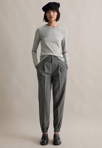 Hellegrau Langarmoberteil kombiniert mit dunkelgrauen, gestreiften, schmal zulaufenden Hosen mit elastischem Bund. Eine schwarze Baskenmütze und klobige schwarze Schuhe runden das Outfit ab.