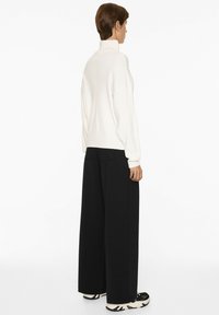 White ribbed turtleneck sweater with long sleeves, paired with high-waisted, wide-leg black trousers. The outfit features sneakers with patterns.