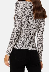 Långärmad topp i ljus kräm med svart blommönster, figurnära design och textilåtergivning, matchad med svarta jeans.