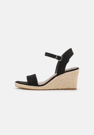 Sort kilehæl sandal med ankelrem, flettet jutesål og åben tå, sat mod en hvid baggrund.