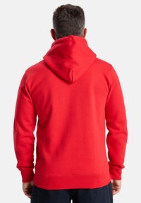 Červená mikina s kapucňou a šnúrkou, so ribbenými manžetami a lemom. Mäkkučká tkanina, predná časť má klokanie vrecko a nie sú viditeľné žiadne logá.