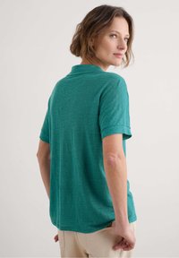 Teal short-sleeve polo shirt with a soft texture and a classic collar, featuring a relaxed fit that drapes at the back.