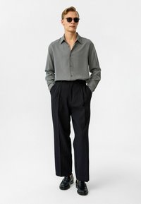 Grijze overhemd met kraag, gecombineerd met zwarte geplooide broek en zwarte schoenen. Gladde stofstructuur, relaxed fit, geen patronen.