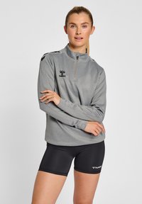 Grå kvartdraget sportspullover med svart logotyp och detaljer, kombinerad med svarta shorts. Har en mjuk textur och atletisk passform.